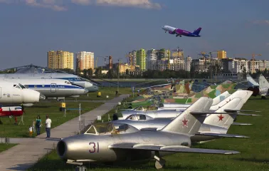 Aviation Museum in Kyiv - row of vintage silver military jets parked on the grass with a modern Wizz Air passenger plane taking off in the blue sky