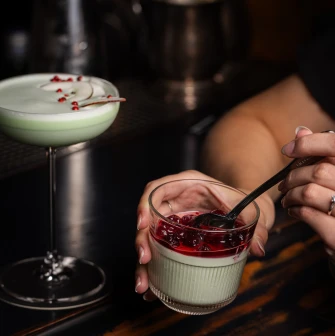 A cocktail in a glass and a dessert in a glass with berry topping