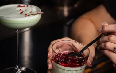 A cocktail in a glass and a dessert in a glass with berry topping