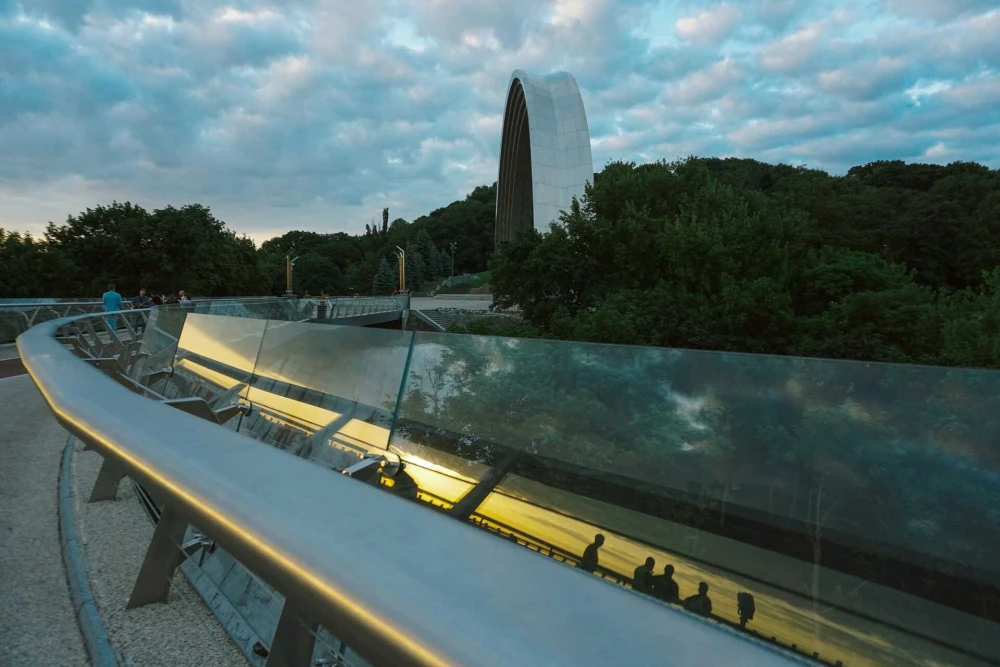 Glass railing of a bridge overlooking the Dnipro River and Kyiv hills