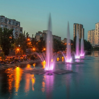 Rusanivska Naberezhna in Kyiv - vibrant evening scene featuring a row of illuminated purple and pink fountains spraying high into the air
