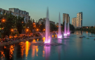 Rusanivska Naberezhna in Kyiv - vibrant evening scene featuring a row of illuminated purple and pink fountains spraying high into the air
