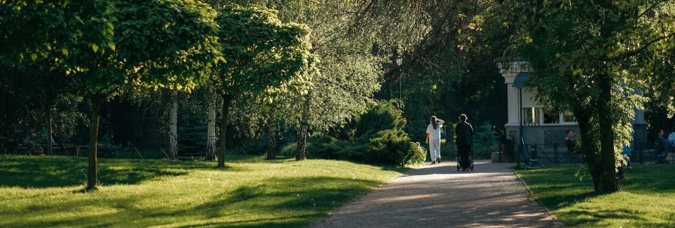 People walking on a path in a sunlit green park with trees in VDNG