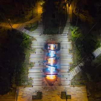 Park Partyzanskoi Slavy in Kyiv - aerial night view of the park's central alley featuring the glowing geometric fountain complex surrounded by dark forest trees
