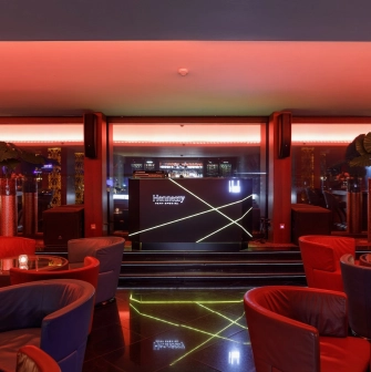 B-hush Lounge Bar – stylish interior with red and blue armchairs, glowing bar counter and panoramic evening lighting