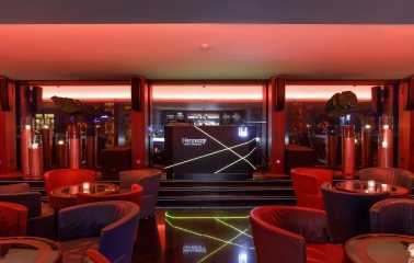 B-hush Lounge Bar – stylish interior with red and blue armchairs, glowing bar counter and panoramic evening lighting