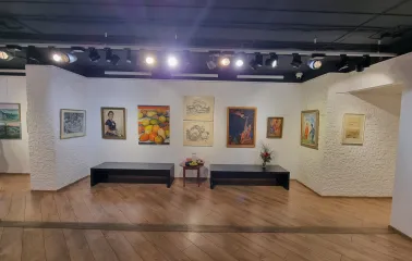 Muzei Suchasnoho Mystetstva in Kyiv - exhibition space with warm lighting featuring a collection of paintings, black benches for rest, and white textured walls