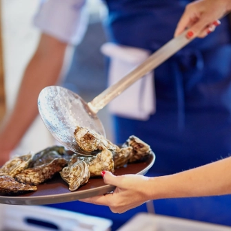 Restaurant Prychal - chef placing fresh raw oysters onto a serving plate with a slotted spoon