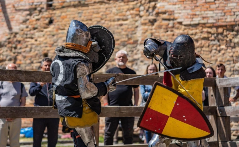 Medieval knights in full armor jousting on horseback during the IMCF World Championship in Kyiv, with colorful medieval banners and spectators in period costume