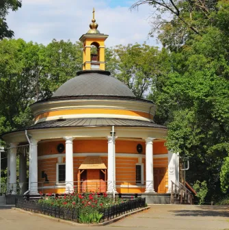 Askoldova Mohyla in Kyiv - iconic St. Nicholas Rotunda Church featuring bright yellow walls and white columns nestled among the peaceful park trees