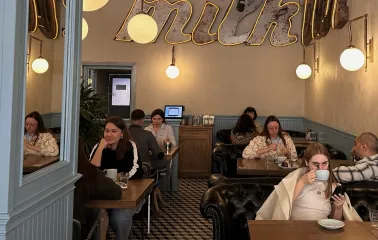 Milk Bar - cozy cafe interior with guests enjoying coffee under neon milk sign