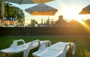 Lounge area with sun loungers near the volleyball court and pool among trees