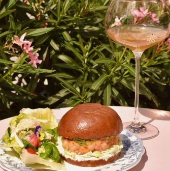 Namelaka - salmon burger with fresh salad and wine glass on pink table