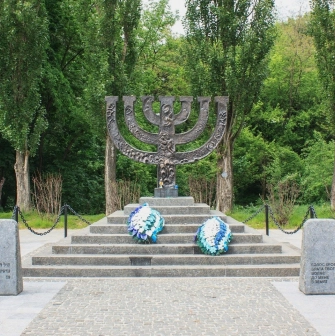 Babyn Yar in Kyiv - solemn Menorah monument standing on a stone pedestal surrounded by forest trees honoring the Jewish victims