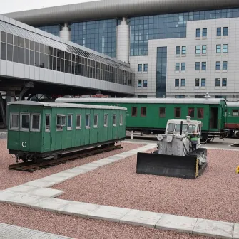 Railway Museum in Kyiv - outdoor exhibition of vintage green railway carriages parked on gravel tracks near the modern glass train station building
