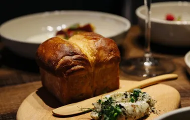 Chef’s Table — brioche bread with herb butter served on a wooden board and glass of wine
