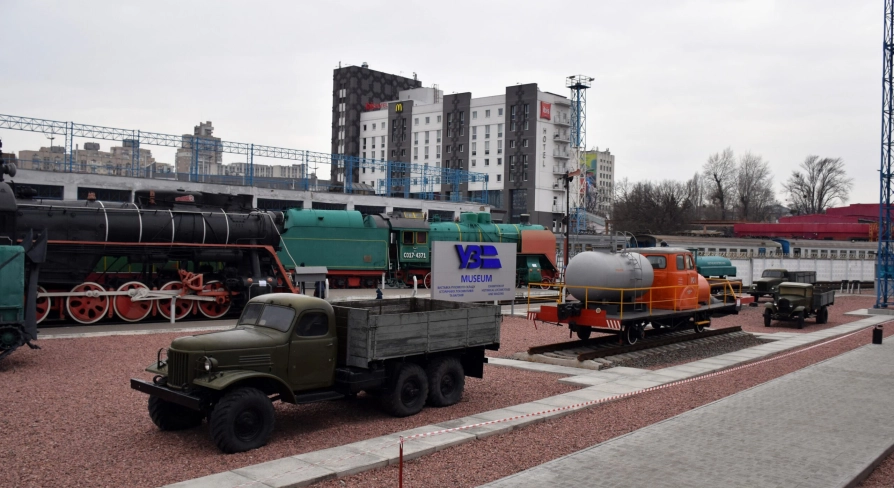 Railway Museum in Kyiv - open-air museum grounds displaying a variety of black steam engines, green locomotives, and vintage trucks on red gravel