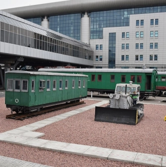 Railway Museum in Kyiv - outdoor exhibition of vintage green railway carriages parked on gravel tracks near the modern glass train station building