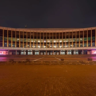 Palats Ukraina in Kyiv - panoramic night view of the illuminated curved glass facade decorated with festive pink banners