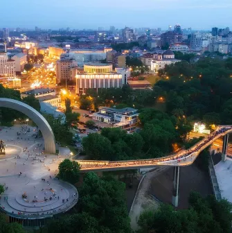 Aerial night view of the illuminated Glass Bridge and Arch of Freedom in Kyiv