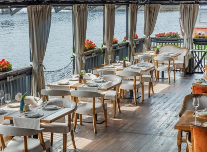 Restaurant Khutorets na Dnipri - waterfront terrace with white dining chairs and river view