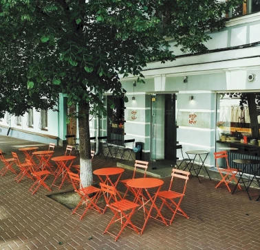 Svit Kavy in Kyiv - outdoor terrace with red folding tables and chairs under trees
