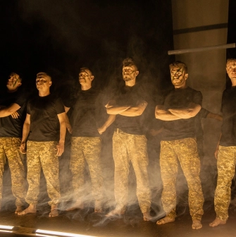 Teatr Voiennykh Dii in Kyiv - powerful lineup of actors in military trousers standing in stage smoke under dramatic side lighting