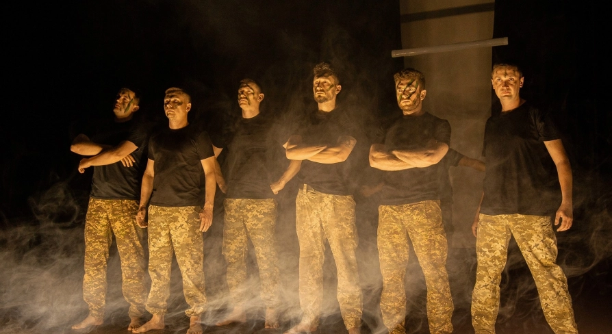 Teatr Voiennykh Dii in Kyiv - powerful lineup of actors in military trousers standing in stage smoke under dramatic side lighting