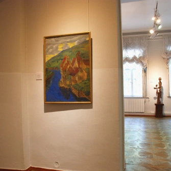 Kyivska Kartynna Halereia in Kyiv - bright landscape painting hanging on a white wall near a small wooden sculpture