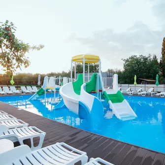 Outdoor swimming pool with bright children's slides and rows of white sun loungers around it