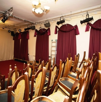 Teatr Koleso in Kyiv - small theater auditorium with rows of wooden chairs and red heavy curtains