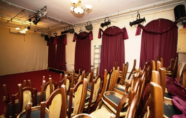 Teatr Koleso in Kyiv - small theater auditorium with rows of wooden chairs and red heavy curtains
