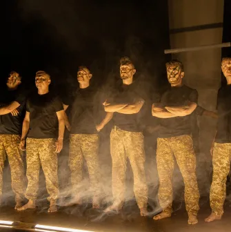 Teatr Voiennykh Dii in Kyiv - powerful lineup of actors in military trousers standing in stage smoke under dramatic side lighting