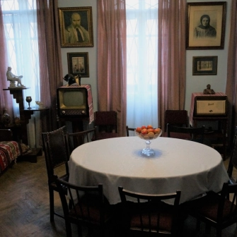 Muzei Tychyny in Kyiv - dining room area featuring a round table with apples, vintage furniture, a retro television set, and portraits on the light blue walls