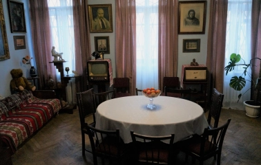 Muzei Tychyny in Kyiv - dining room area featuring a round table with apples, vintage furniture, a retro television set, and portraits on the light blue walls
