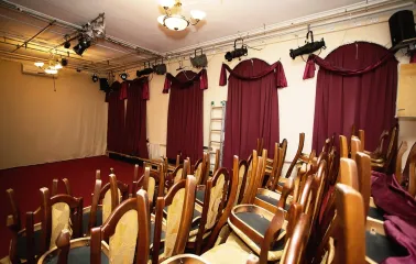 Teatr Koleso in Kyiv - small theater auditorium with rows of wooden chairs and red heavy curtains