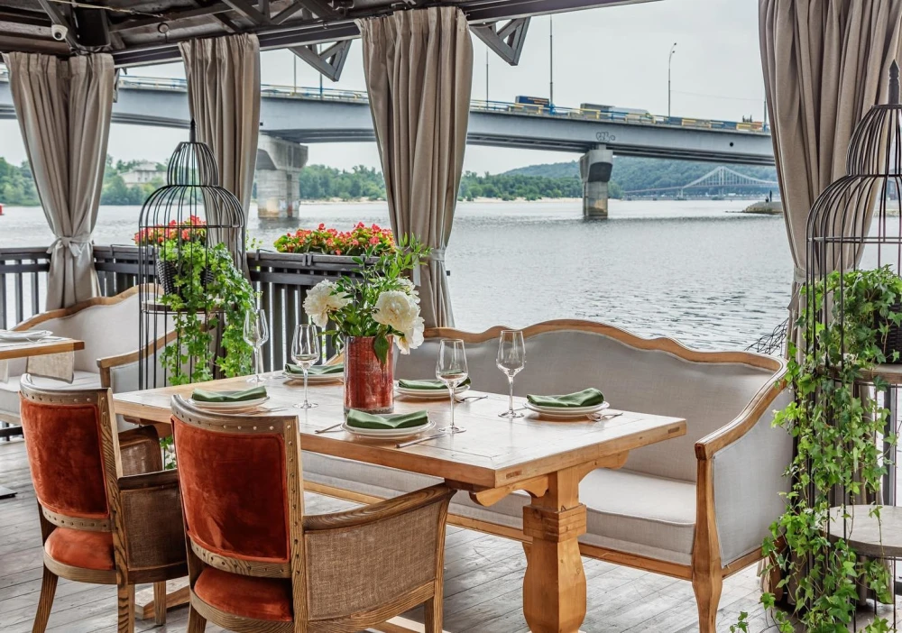 Khutorets na Dnipri – elegant wooden table with green napkins on the river terrace overlooking the Dnipro and bridge