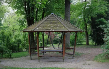 Park Partyzanskoi Slavy in Kyiv - rustic hexagonal wooden gazebo with a tiled roof standing in a secluded shady spot among green trees
