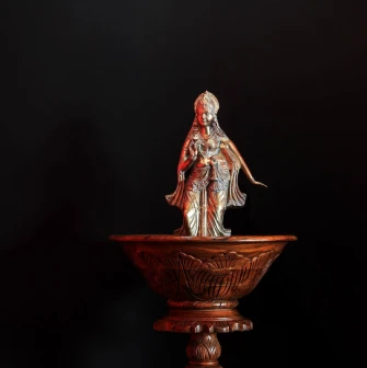 Bronze deity figurine in a wooden bowl against a black background