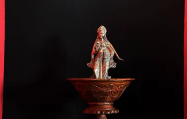 Bronze deity figurine in a wooden bowl against a black background
