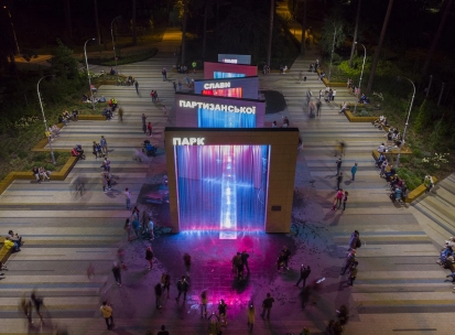 Park Partyzanskoi Slavy in Kyiv - spectacular evening view of the illuminated pedestrian fountains with towering arches cascading water in bright lights surrounded by visitors
