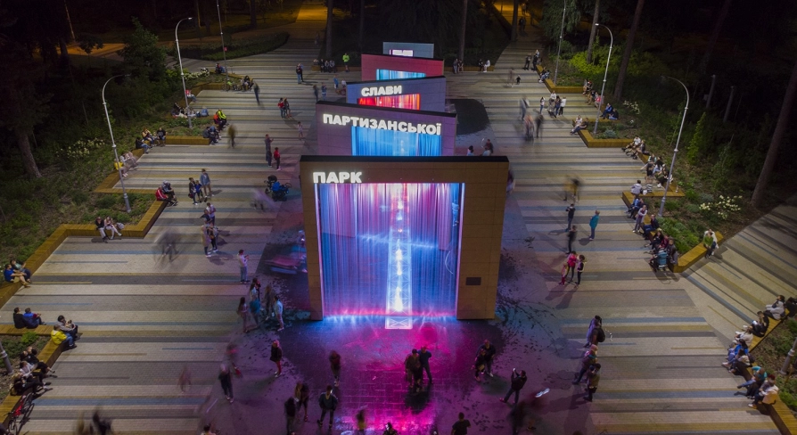 Park Partyzanskoi Slavy in Kyiv - spectacular evening view of the illuminated pedestrian fountains with towering arches cascading water in bright lights surrounded by visitors