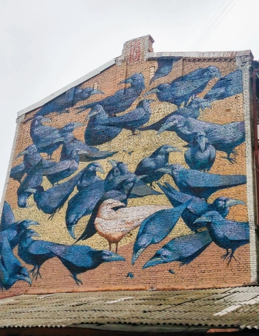 Messenger of Life in Kyiv - mural of white crow among flock, symbolizing that being unique is the norm