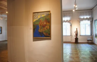 Kyivska Kartynna Halereia in Kyiv - bright landscape painting hanging on a white wall near a small wooden sculpture