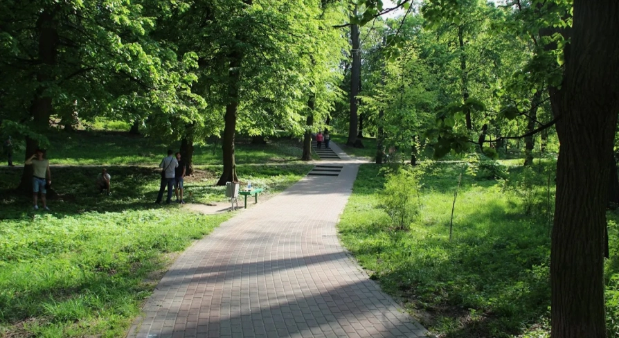 Park Kyn-Grust - shady alley with a paved path and stairs leading up a hill with people walking
