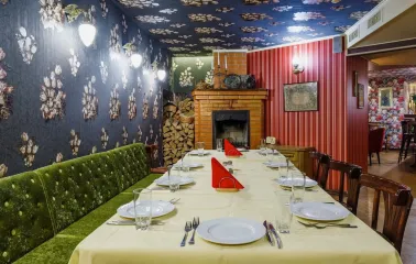 Restaurant Za Dvoma Zaicyamy - long dining table set in a room with a fireplace woodpile and patterned walls