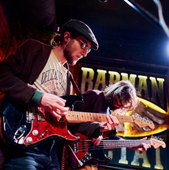 BarmanDictat - two musicians playing electric and bass guitars on a small stage