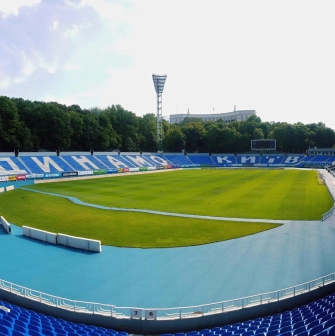 Dynamo Stadium in Kyiv - panoramic view from the stands showing the green pitch and blue seats with "Dynamo" and "Kyiv" lettering