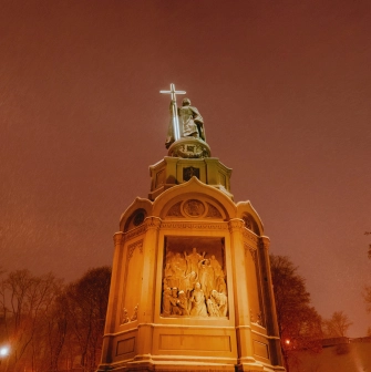 Monument to Vladimir the Great - illuminated statue holding a glowing cross on a snowy winter night