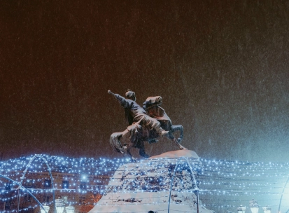 Monument to Bogdan Khmelnytsky in Kyiv - illuminated equestrian statue standing above festive Christmas lights on a snowy night
